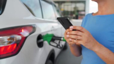 Arabası yakıt ikmali yaparken akıllı telefon kullanan bir kadın.