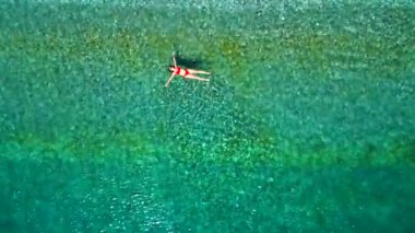 Kırmızı mayo giymiş bir kadının hava görüntüsü, kristal berrak deniz sularında rahatlama somutlaştırıcı bir şekilde sırtüstü uzanır. Yaz tatilleri.