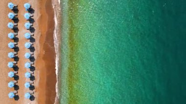 Mavi güneş şemsiyeleri ve turkuaz deniz suyuyla cennet gibi kumlu sahil manzarası..