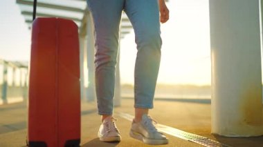 Kadın yalnız seyahat ediyor. Bir gezgin gün batımında şık kahverengi bavullarıyla havaalanı terminalinde geziniyor. Yaz tatili kavramı. Yavaş çekim.