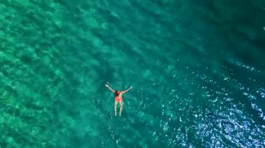 Pembe mayo giymiş bir kadının hava görüntüsü kristal berrak deniz sularında yüzüyor, rahatlatıcı bir şekilde. Yaz tatilleri.