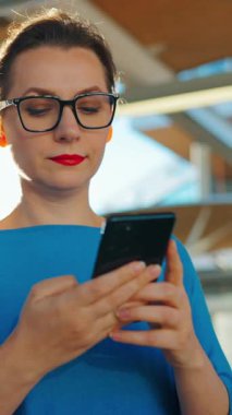 Kadın toplu taşıma durağında duruyor, akıllı telefon kullanıyor ve treni bekliyor. Ağır çekim. Şehir, şehir, ulaşım. 