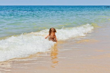 Sahilde oturan ve dalgalar halinde oynarken küçük bebek kız. Khao Lak Plajı. Tayland