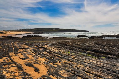 Mavi gökyüzünün altındaki plajda kaya oluşumları