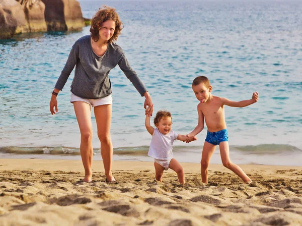 Ung kvinna med sin dotter och son som leker på stranden — Stockfoto