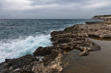 Kasvetli bir dramatik gökyüzü altında kayalık plaj
