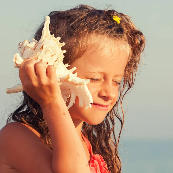 孩子把贝壳放在她的耳朵上 海上女孩背景 — 图库照片