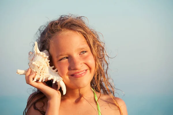 海を背景に少女 子供はその貝を耳に入れた 夏休み — ストック写真