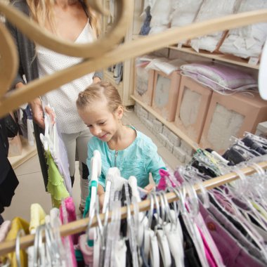 Çocuk dükkanında annesi olan bir çocuk. Kıyafet seçen mutlu kız. Aile alışverişte.