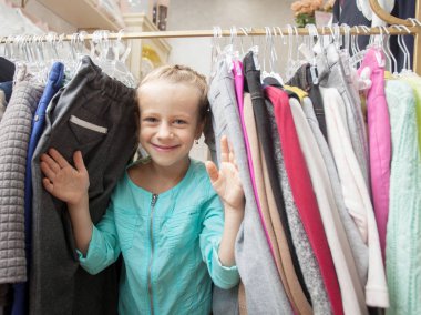 Çocuk mağazasında bir çocuk. Mutlu kız kıyafet seçiyor.