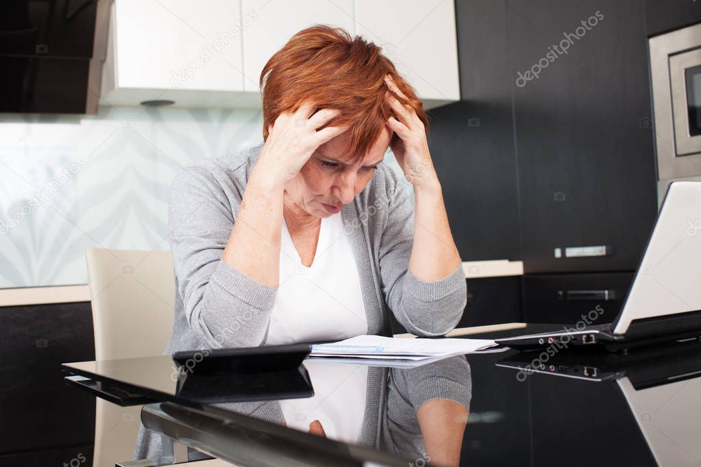 Elderly woman sorting through her old receipts at home. Sad businesswoman with document