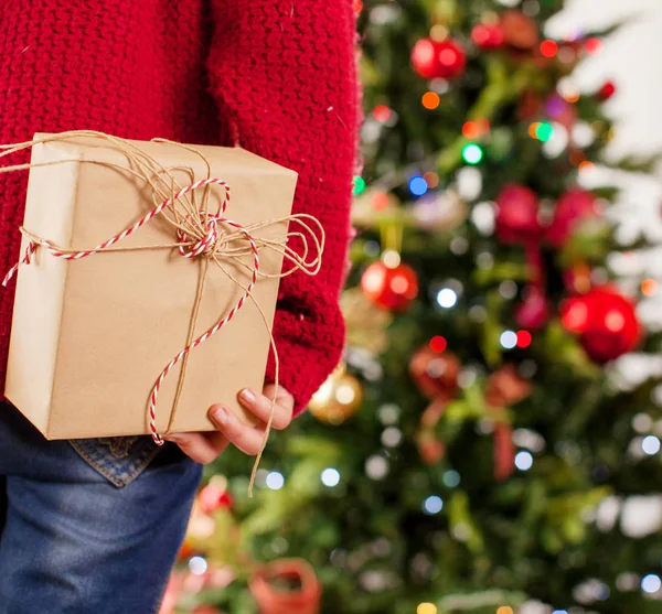 Child near the Christmas tree with a gift behind — Stock Photo, Image