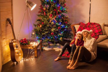 Gülümseyen kız ve annesi evde Noel ağacının yanında.