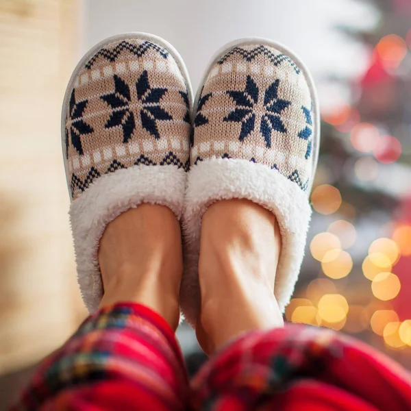 Pernas em chinelos no fundo da árvore de Natal — Fotografia de Stock