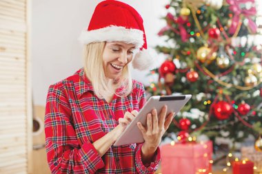 Yılbaşı ağacının önünde tablet kullanan kadın.