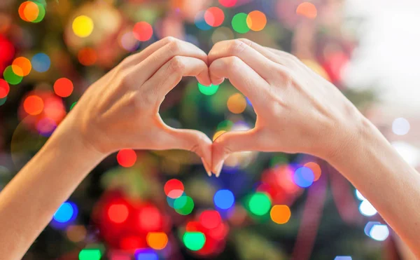 Herz aus den Händen vor dem Weihnachtsbaum — Stockfoto