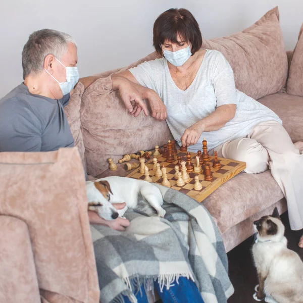パンデミックコロナウイルス中の医療マスクの高齢者のカップルはチェスをする — ストック写真
