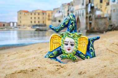 Traditional sicilian souvenir - ceramic Trinacria on a sandy beach in Cefalu. Sicily, Italy clipart