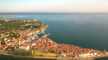 4k. Altın gün batımında eski şehir Piran üzerinde uçuş, eski evler, Tartini Meydanı, St George's Parish Kilisesi, kale ve marina ile havadan panoramik görünümü.