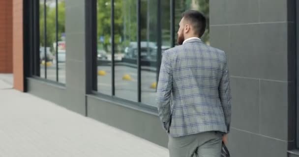 Ein junger, gutaussehender Geschäftsmann, Student im Anzug, kommt mit einer Aktentasche, am Bahnhof, am Flughafen oder im Business Center. Rückansicht — Stockvideo