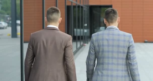 Twee zakenlieden chatten samen als ze langs via een drukke moderne kantoorgebouw lopen. Achteraanzicht — Stockvideo