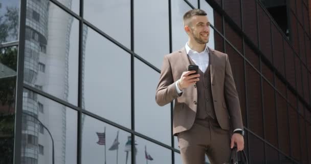 Empresario usando su teléfono inteligente. Joven guapo comunicándose en el teléfono inteligente sonriendo confiado — Vídeos de Stock