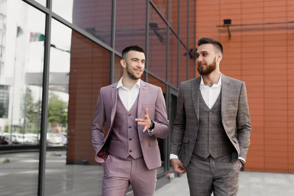 İki genç işadamları yürüyüş gülümseyen ve şehirde konuşuyor