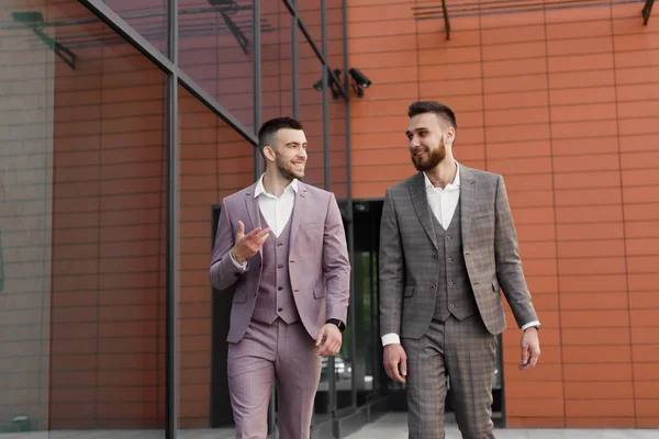 İki genç işadamları yürüyüş gülümseyen ve şehirde konuşuyor