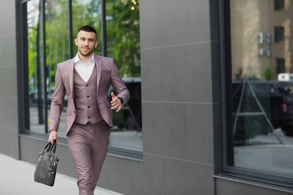 Молодой бизнесмен с портфелем, бегущим по городской улице на фоне стены — стоковое фото