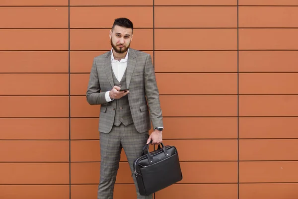 Hombre de negocios con traje y el uso de un teléfono inteligente moderno cerca de la oficina en la mañana temprano, empleador exitoso para hacer un trato mientras está de pie cerca de rascacielos — Foto de Stock