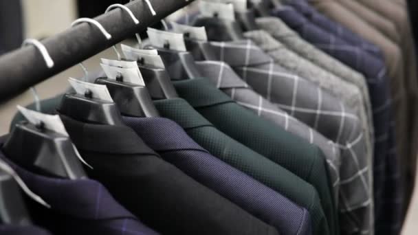 Hanger with mens clothes of different colors against the background of a suit shop, close-up. — Stock Video