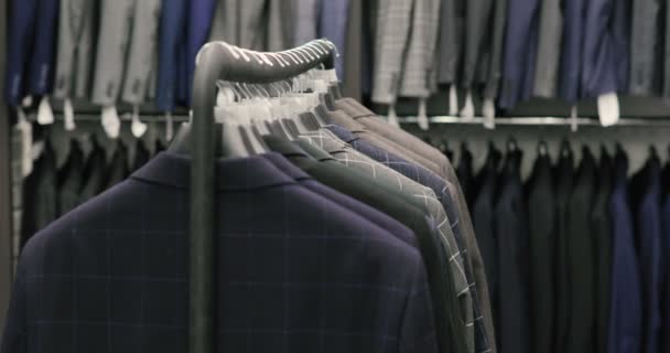 Cintre avec des vêtements pour hommes de différentes couleurs sur le fond d'un magasin de costumes, gros plan . — Video