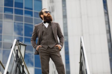 Modern iş adamı. Kendine güvenen genç adam açık havada cityscape arka plan ayakta iken uzak tam takım arıyor