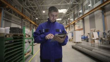 O mavi üniforma giymiş, bir adam bir dijital tablet ile bir fabrikada çalışıyor. fabrika işçisi.