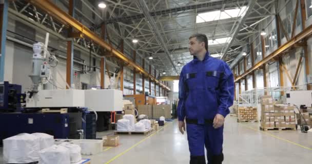 Ingeniero en uniforme azul está caminando a través de fábrica. Vista frontal — Vídeo de stock