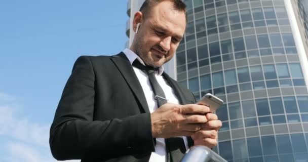 Homem SMS SMS usando aplicativo no telefone inteligente no distrito de negócios da cidade. Jovem homem de negócios usando smartphone sorrindo feliz vestindo jaqueta terno — Vídeo de Stock