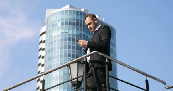 Homem SMS SMS usando aplicativo no telefone inteligente no distrito de negócios da cidade. Jovem homem de negócios usando smartphone sorrindo feliz vestindo jaqueta terno — Vídeo de Stock