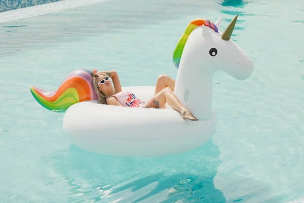 Красива струнка дівчина в купальнику. Плаваючий на великому білому пляжі надувний басейн з єдинорогом — стокове фото
