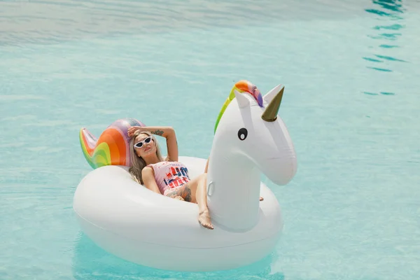 Красива струнка дівчина в купальнику. Плаваючий на великому білому пляжі надувний басейн з єдинорогом — стокове фото