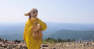 Uzun yürüyüşe çıkan kimse sırt çantası Hiking ile bir dağın tepesinde. kız bir dağın tepesinde bir sarı yağmurluk