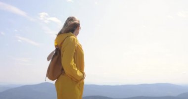 Uzun yürüyüşe çıkan kimse sırt çantası Hiking ile bir dağın tepesinde. kız bir dağın tepesinde bir sarı yağmurluk
