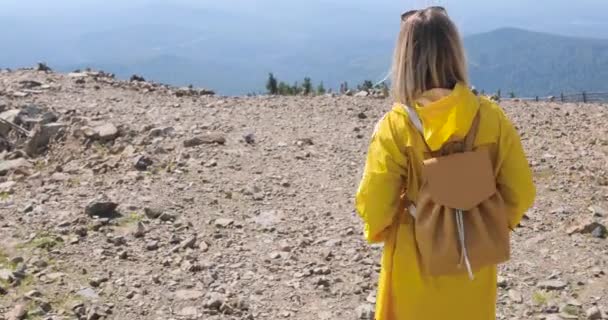 Caminhante com mochila Caminhadas no topo de uma montanha. menina em uma capa de chuva amarela no topo de uma montanha — Vídeo de Stock