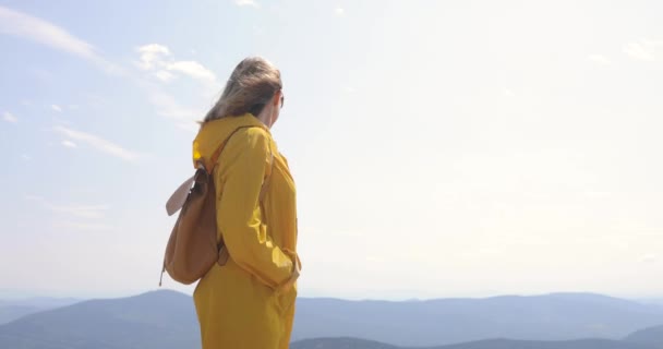Hiker med ryggsäck vandring på toppen av ett berg. flicka i en gul regnrock ovanpå ett berg — Stockvideo