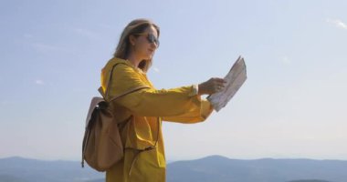 Genç kadın bir dağ iz üzerinde yağmurluk hiking durdurur ve harita yön denetler. Uzun yürüyüşe çıkan kimse dağın tepesine ulaşır, harita üzerinde yön denetler
