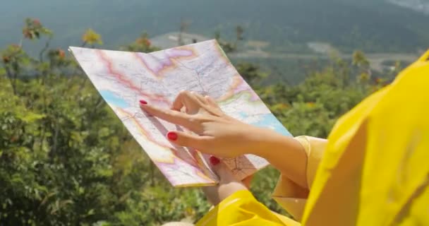 Caminhante em uma capa de chuva amarela olhando para o mapa do topo da montanha. mulher com mapa em montanhas 4k — Vídeo de Stock