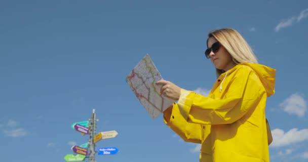 Jonge vrouwelijke wandelen im gele regenjas met een rugzak in bergen bedrijf papieren kaart in handen. — Stockvideo