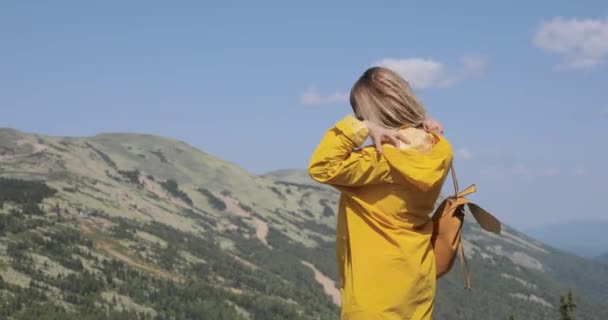 Baksidan på kaukasiska kvinnliga vandrare i gul regnrock står i bergen — Stockvideo