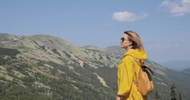 Junge Frau in gelbem Regenmantel steht in den Bergen — Stockvideo
