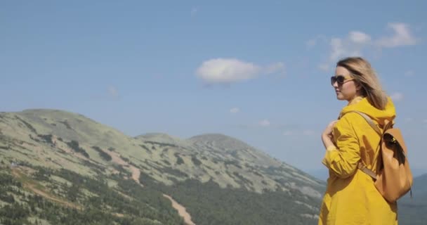 Mladá žena v žlutá pláštěnka stojí v horách — Stock video