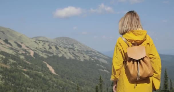 Rückseite einer kaukasischen Wanderin in gelbem Regenmantel steht in den Bergen — Stockvideo